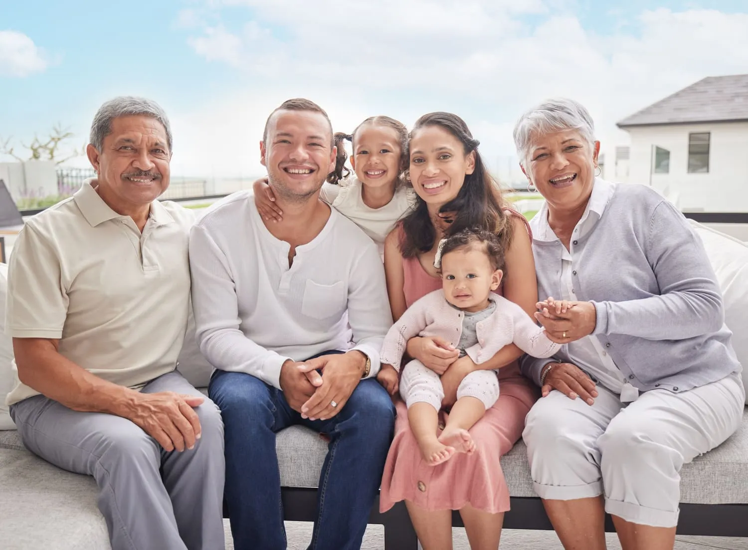 Familia sonriente posando en un sofá, incluyendo dos abuelos, padres y dos niños pequeños, en un ambiente luminoso y acogedor.
